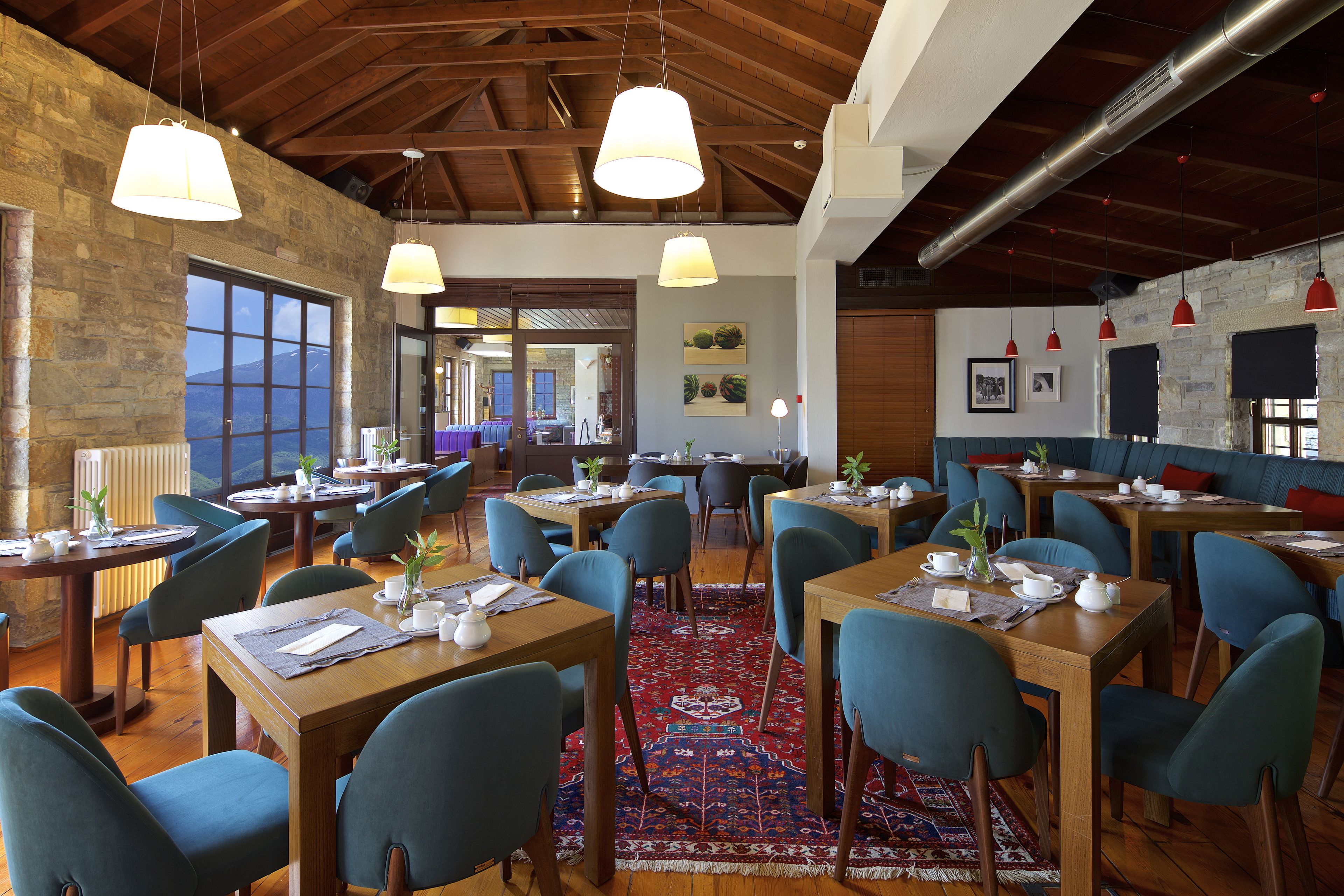 Un restaurant avec des tables en bois et des chaises bleues, des murs en pierre et des lampes suspendues.