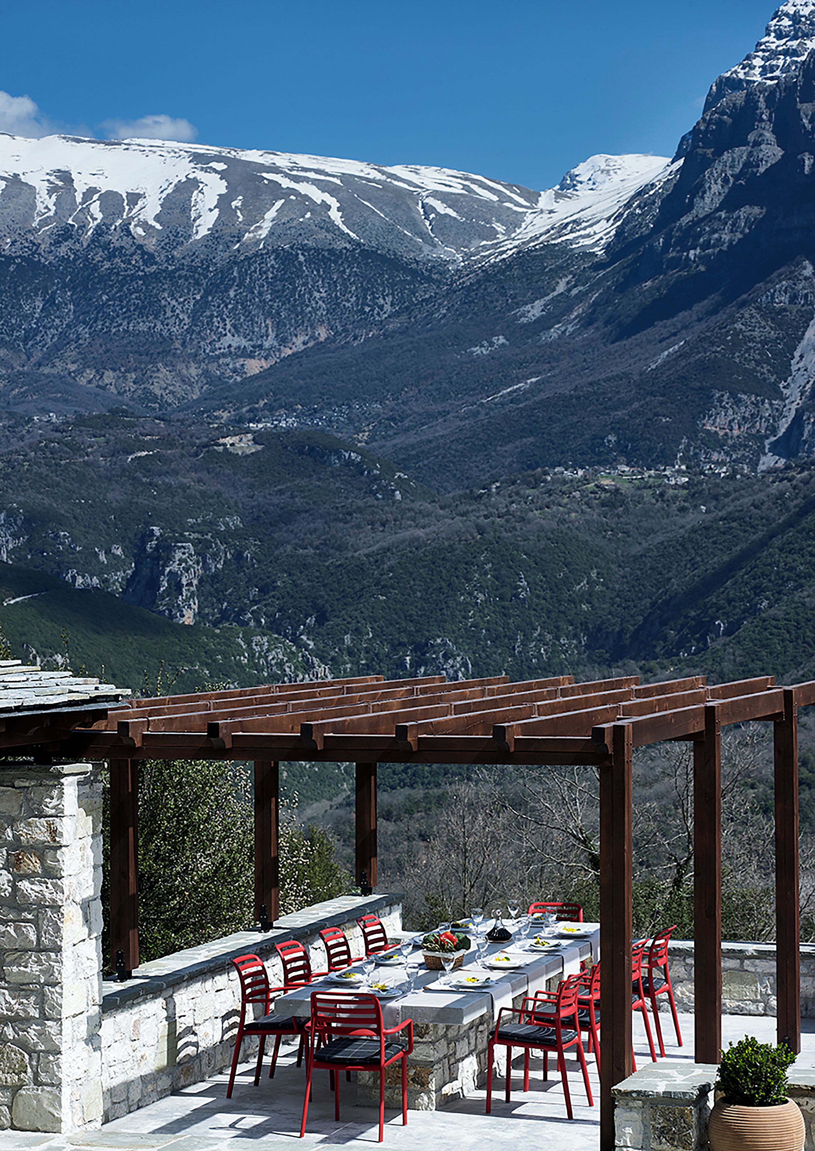Ein Essbereich im Freien mit Steinmauer und Holz-Pergola mit Blick auf schneebedeckte Berge.