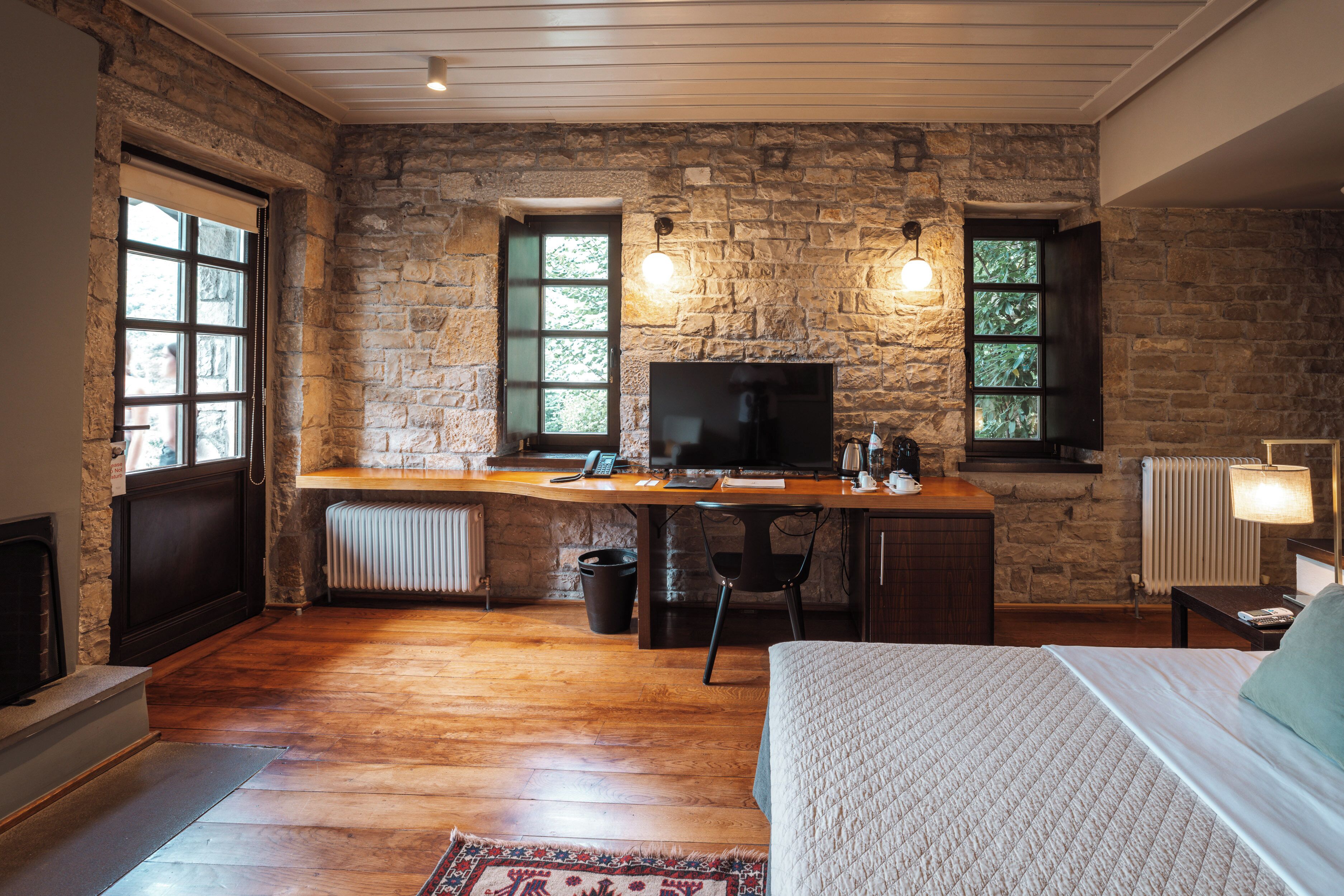 A cozy room with a stone wall, wooden desk, and a bed.