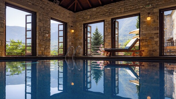 Una piscina con paredes de piedra y amplios ventanales con vistas a las montañas.