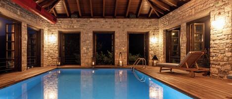 Una piscina con paredes de piedra y vigas de madera, rodeada de puertas y una silla de descanso.