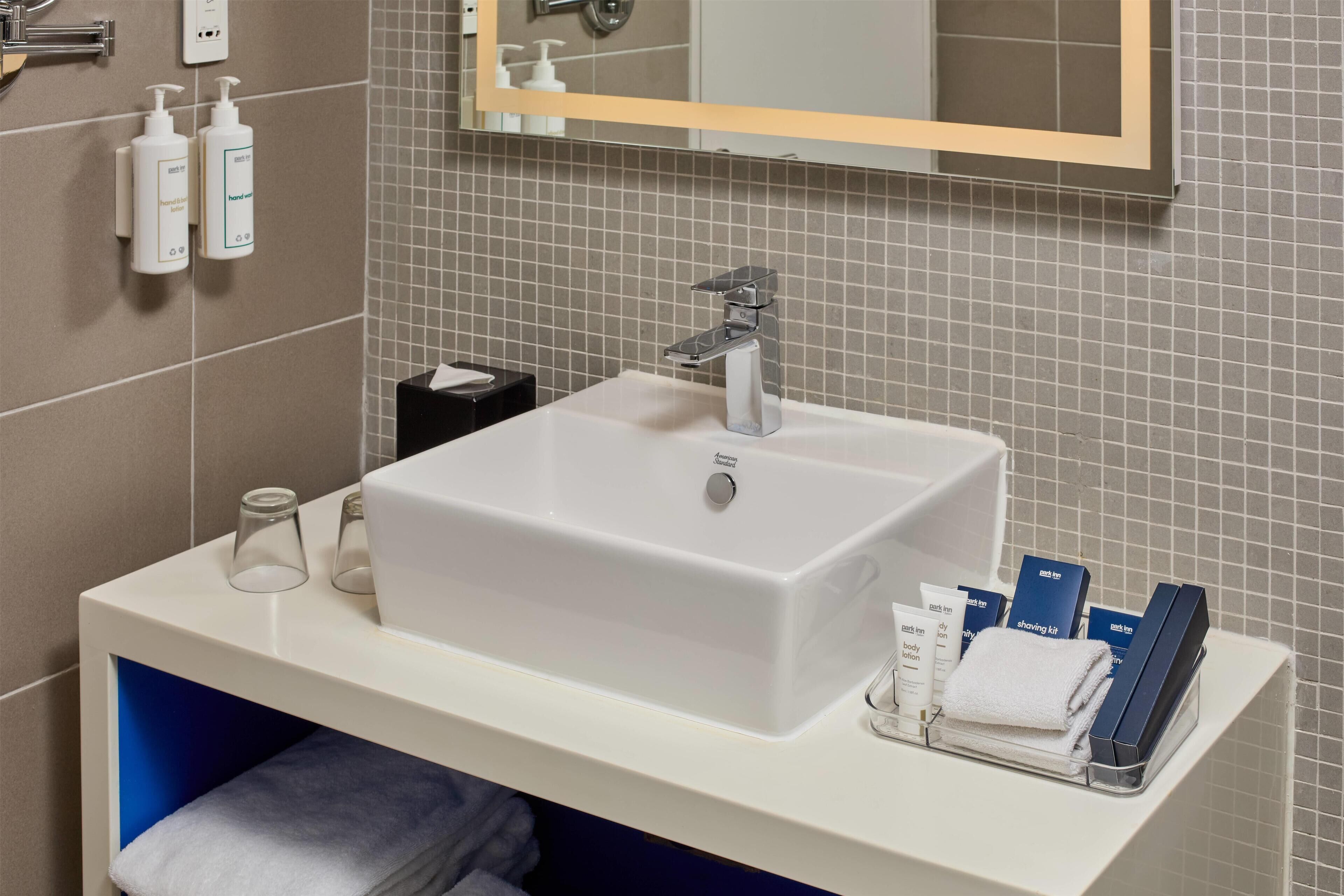 Un baño con un lavabo blanco, un espejo y artículos de aseo en la encimera.