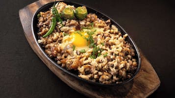 A skillet dish with various ingredients, including green chili peppers and a fried egg, on a wooden board.