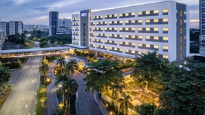 A multi-story hotel with a modern design, featuring a prominent 'Park Inn' sign, a covered walkway, and lush landscaping.