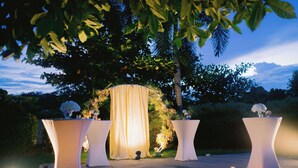 An outdoor wedding setup with a draped arch and tables with candles.
