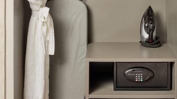 A neatly organized hotel room with a built-in ironing station, a robe hanging on a rack, a pillow, a small bag, and slippers.