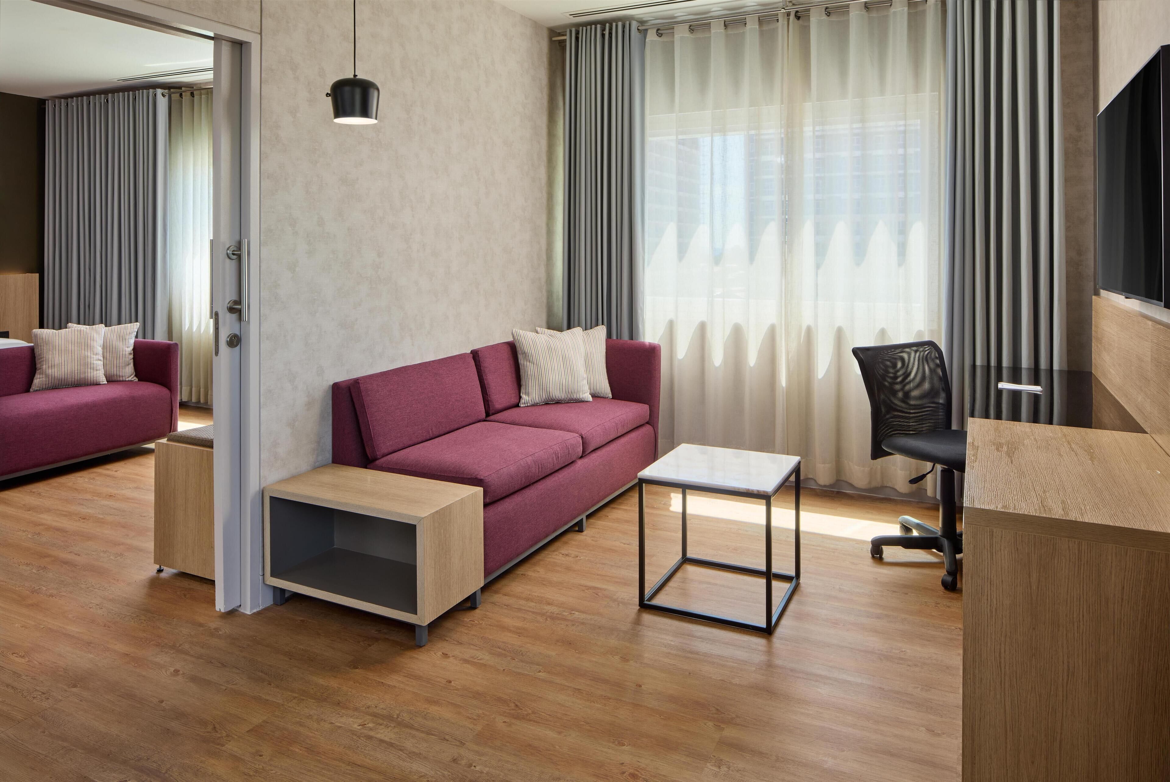 Una sala de estar moderna con un sofá rojo, una pequeña mesa de madera, una silla de oficina negra y un televisor sobre un mueble de madera.