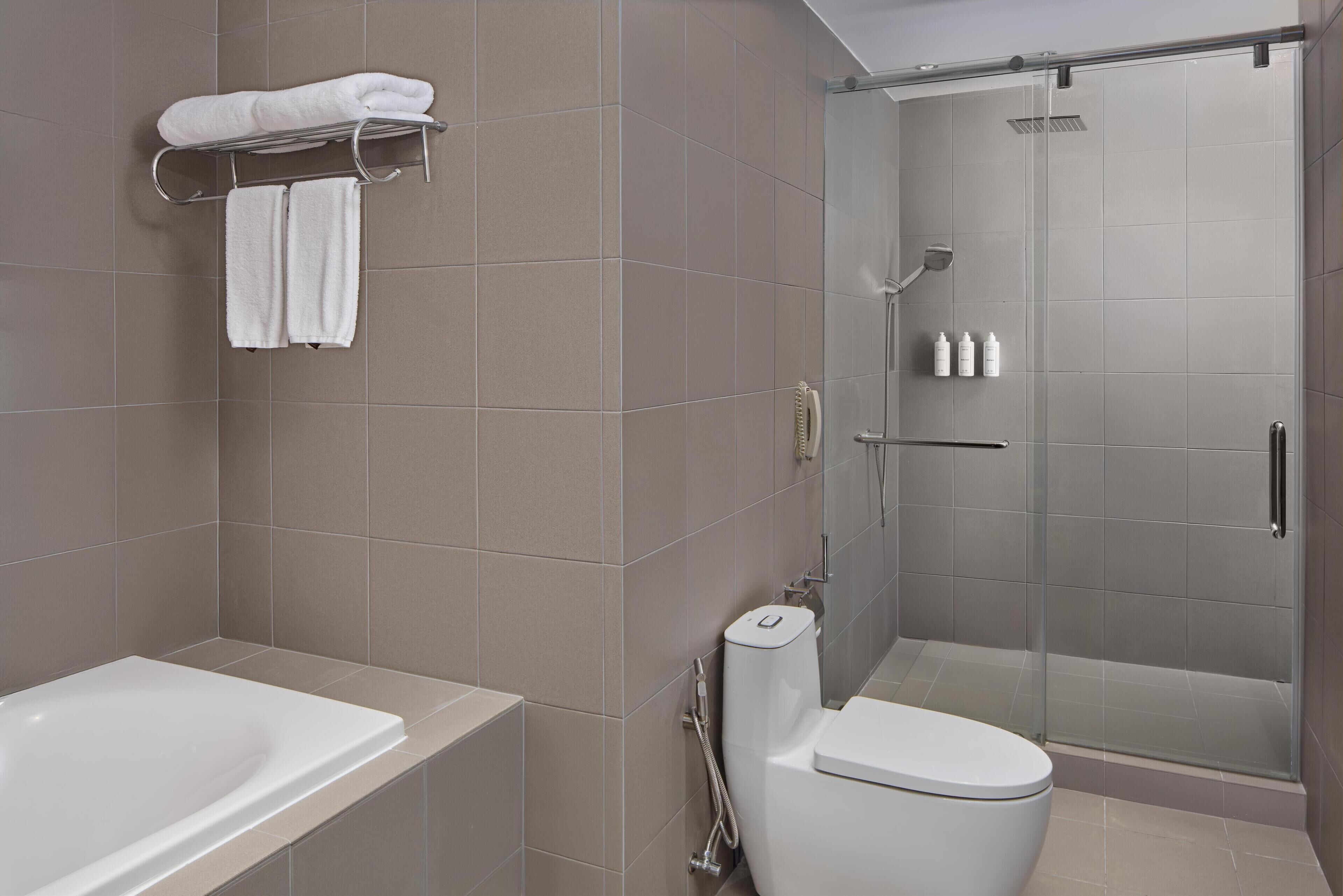 A modern bathroom with a bathtub, toilet, and glass-enclosed shower.