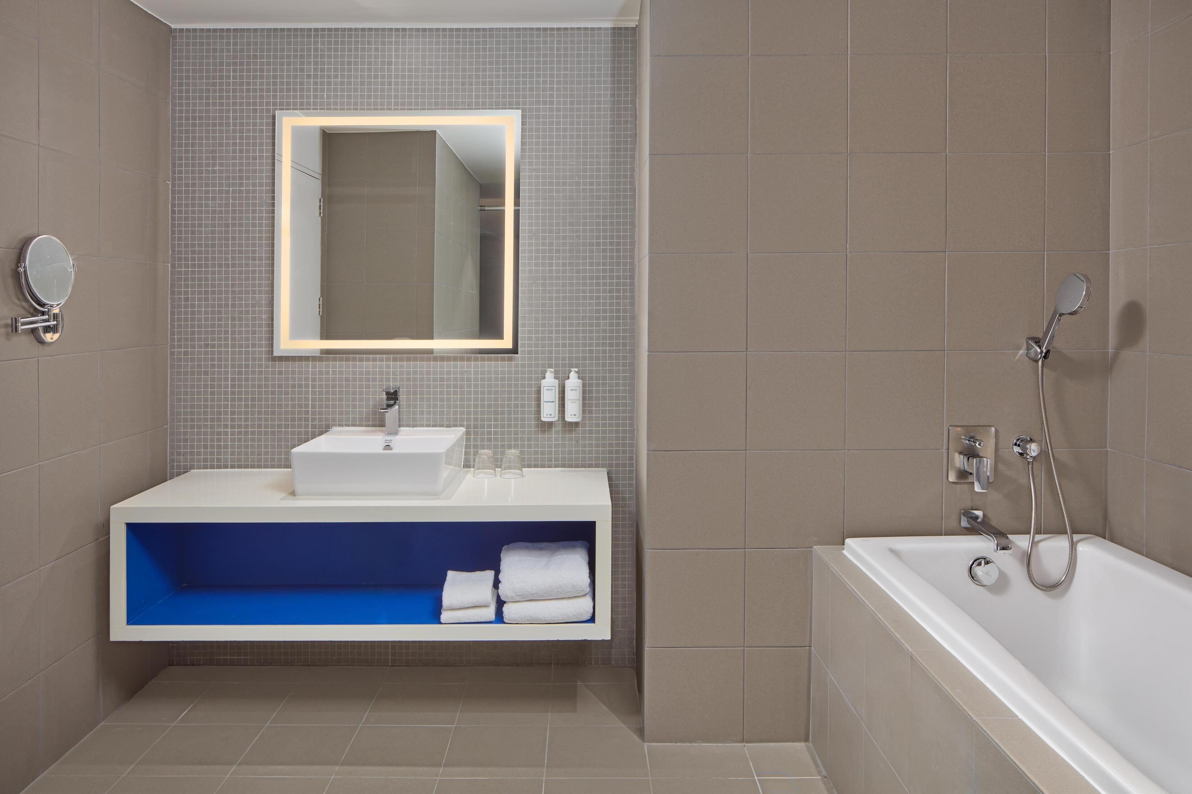 Un baño moderno con un lavamanos blanco, un espejo con luz y una bañera.