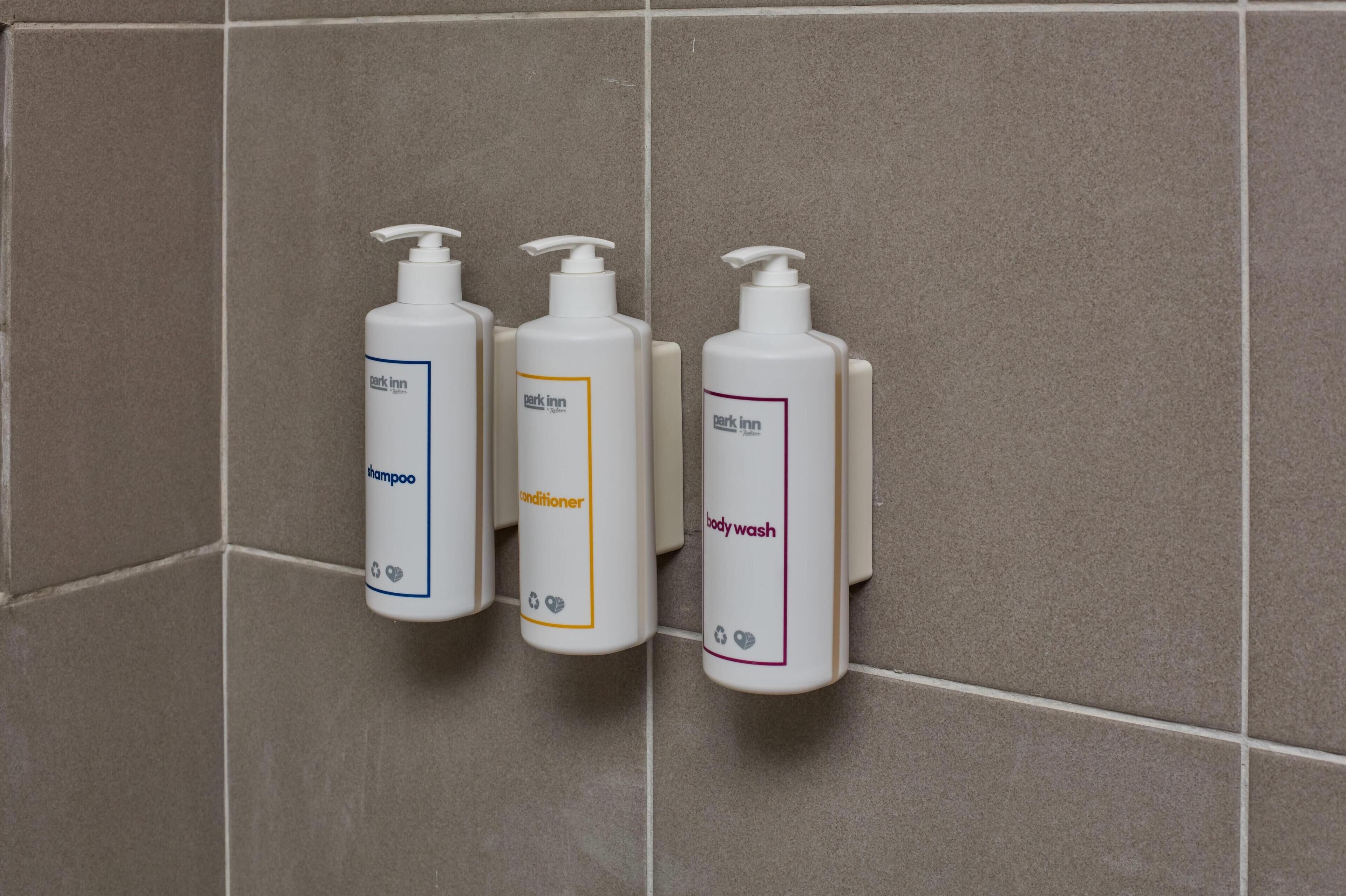 Three bottles of toiletries on a tiled wall.