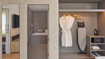 A modern bathroom with a shower, toilet, and sink. There is a robe hanging on a rack and an ironing board.
