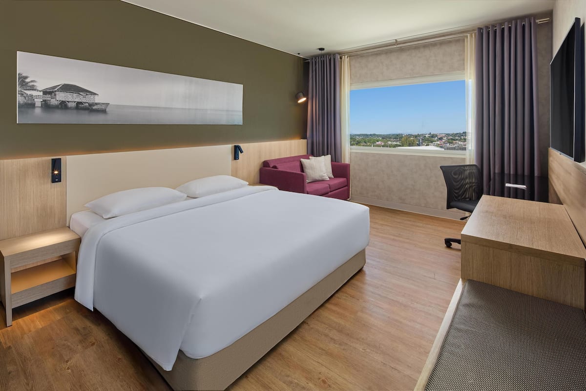 A hotel room with a large bed, a desk, a chair, a sofa, a TV, and a window with a view.