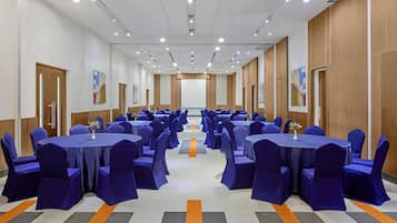 A conference room with multiple tables and chairs, arranged in rows, with a carpeted floor and wooden panel walls.