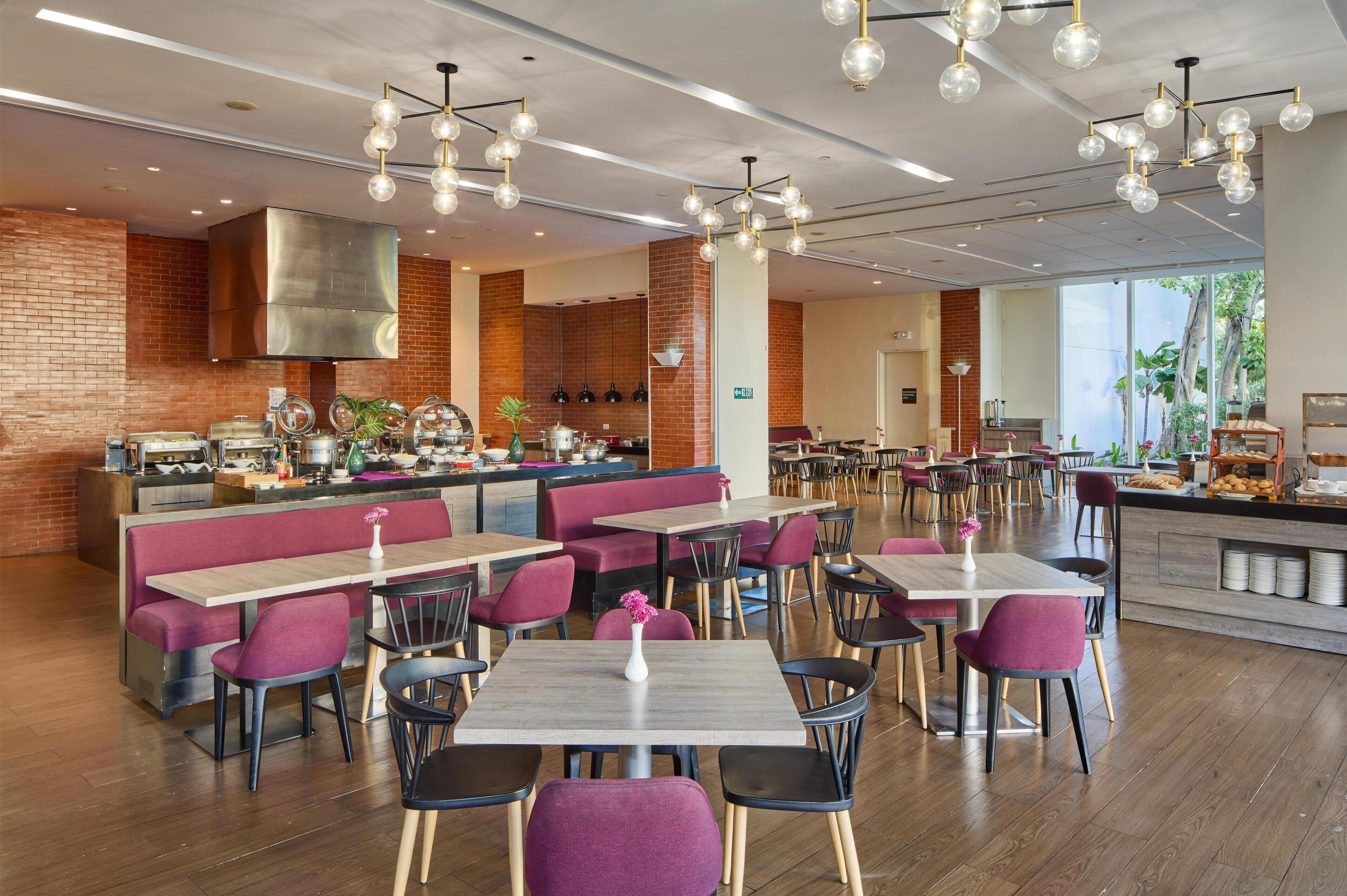 A modern restaurant with booths and tables, a kitchen area, and a view of the outdoors.