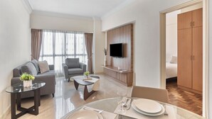 A modern living room with a sofa, coffee table, and TV. There is a dining area with a table set for two.