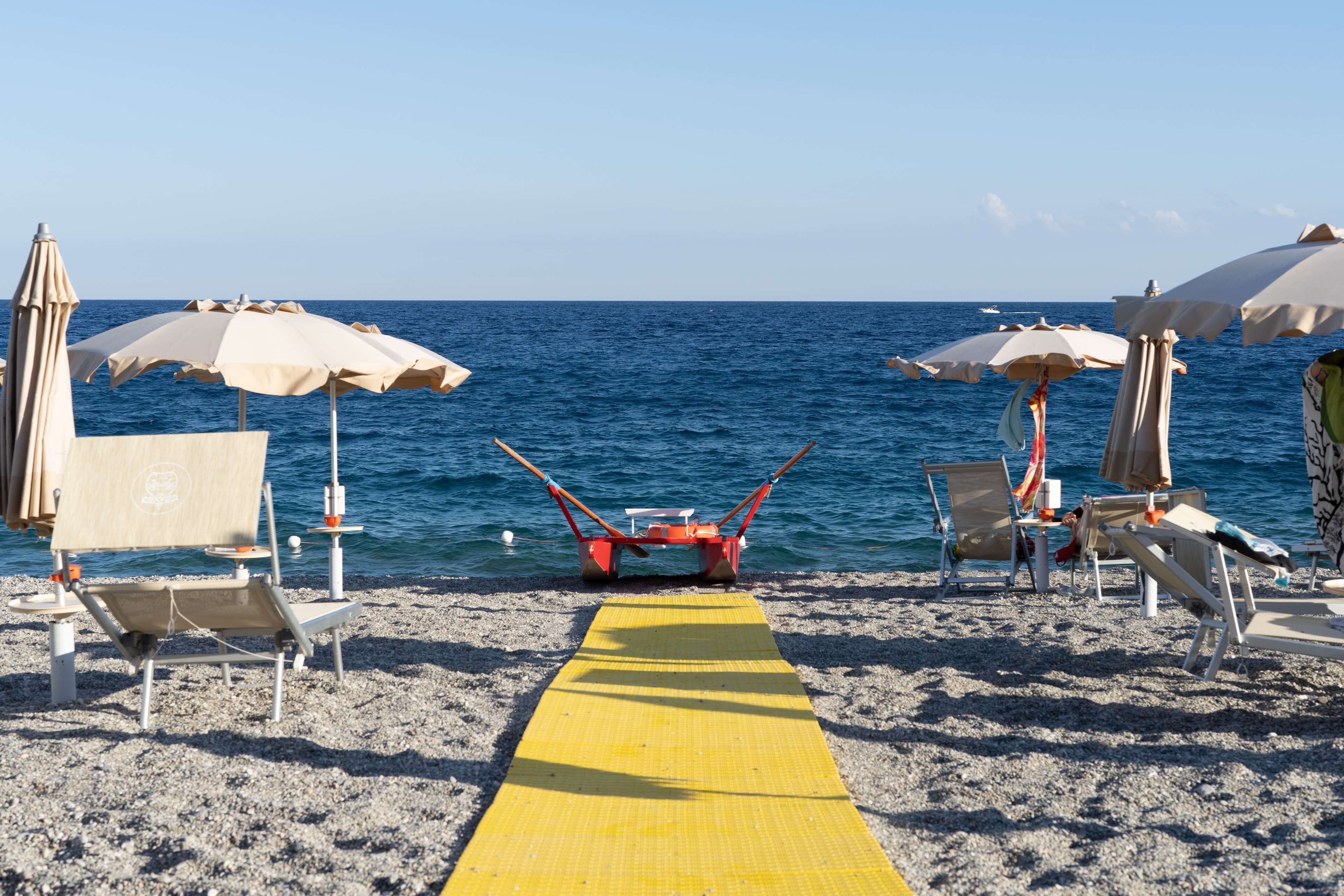 Una spiaggia con un sentiero giallo che conduce al mare, circondata da lettini e ombrelloni.
