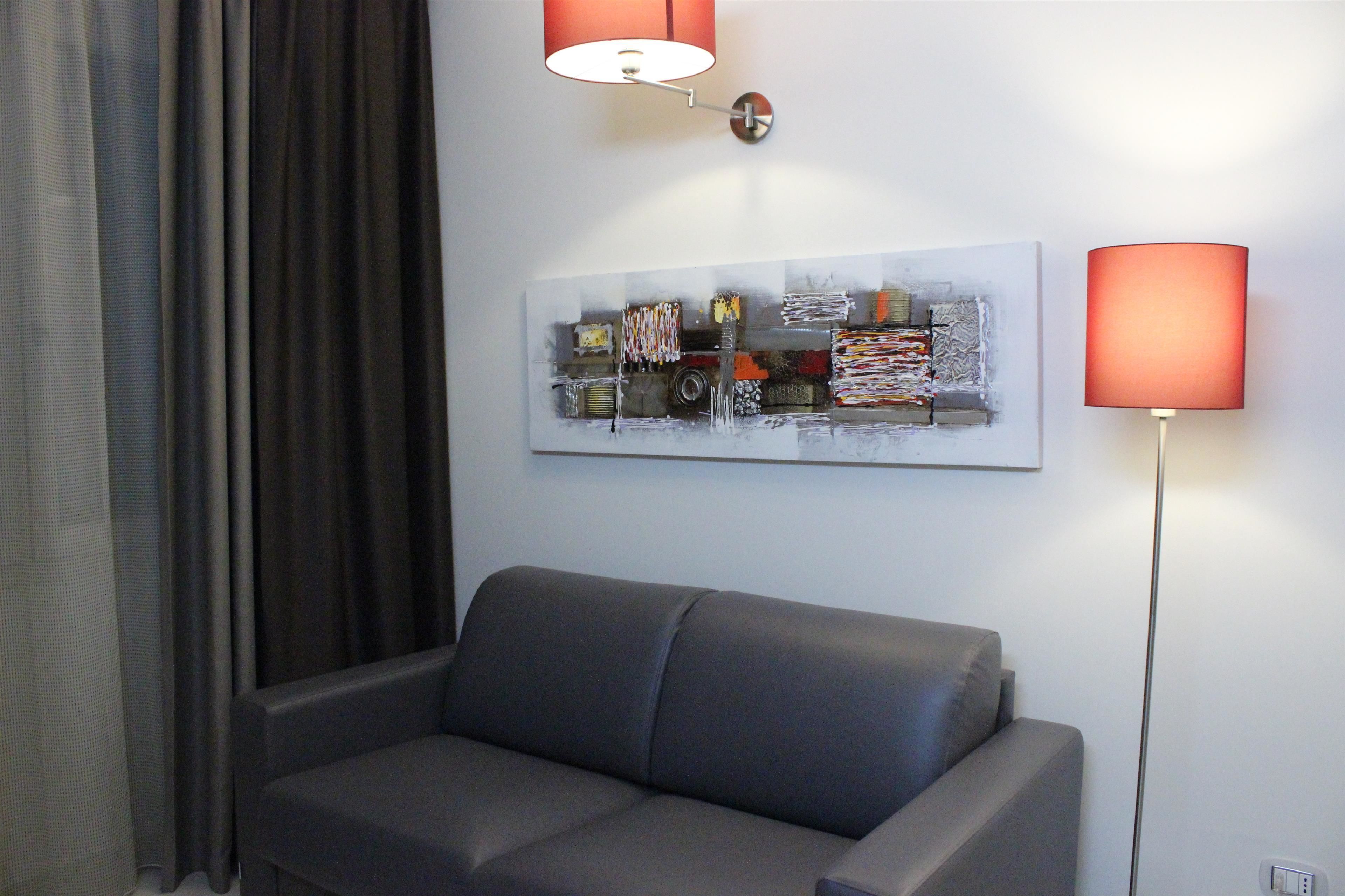 A modern living room with a grey sofa, a contemporary abstract painting, and two floor lamps.