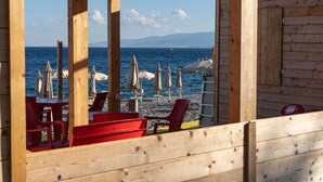 Una cabaña de playa de madera con sillas rojas y sombrillas blancas, con vista al mar.