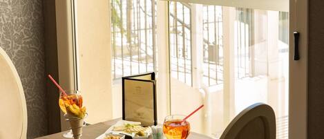 Una mesa de comedor con dos bebidas y un menú, con vistas a un balcón sobre un puerto deportivo.