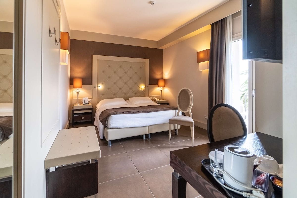 A hotel room with a bed, bedside tables, a desk with a coffee maker, and a chair.
