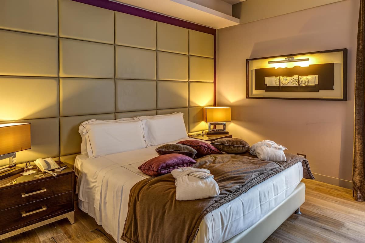 A neatly made bed with a headboard, bedside tables with lamps, and a wall-mounted artwork.