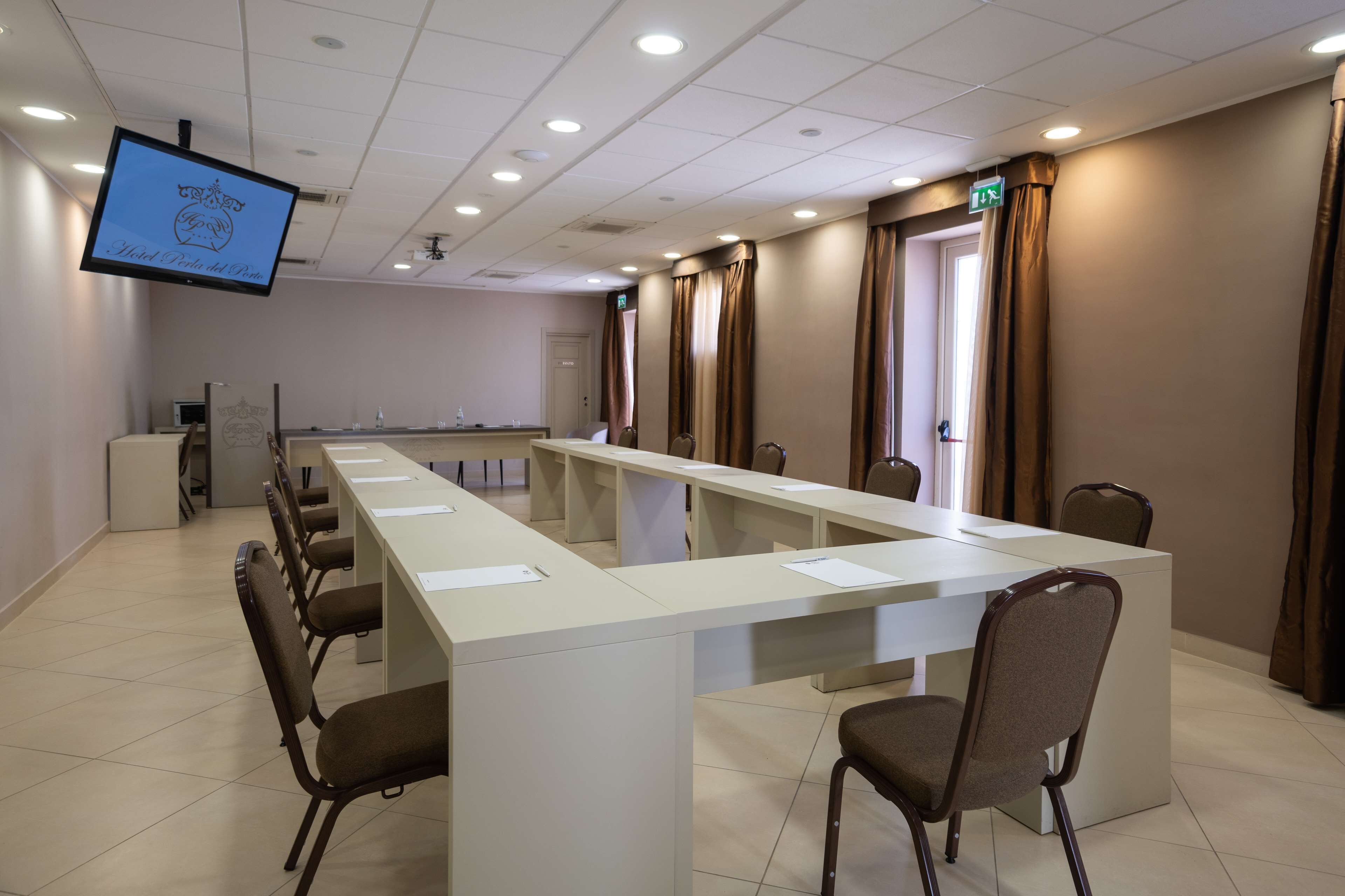 Een vergaderzaal met een lange tafel, stoelen, een scherm en gordijnen.
