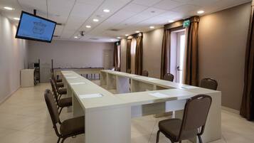 Uma sala de conferência com uma mesa comprida, cadeiras, uma tela e cortinas.