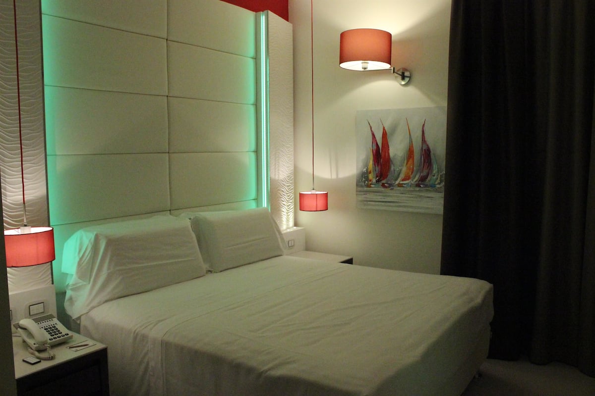 A hotel room with a large bed, a bedside telephone, and two wall-mounted lamps.