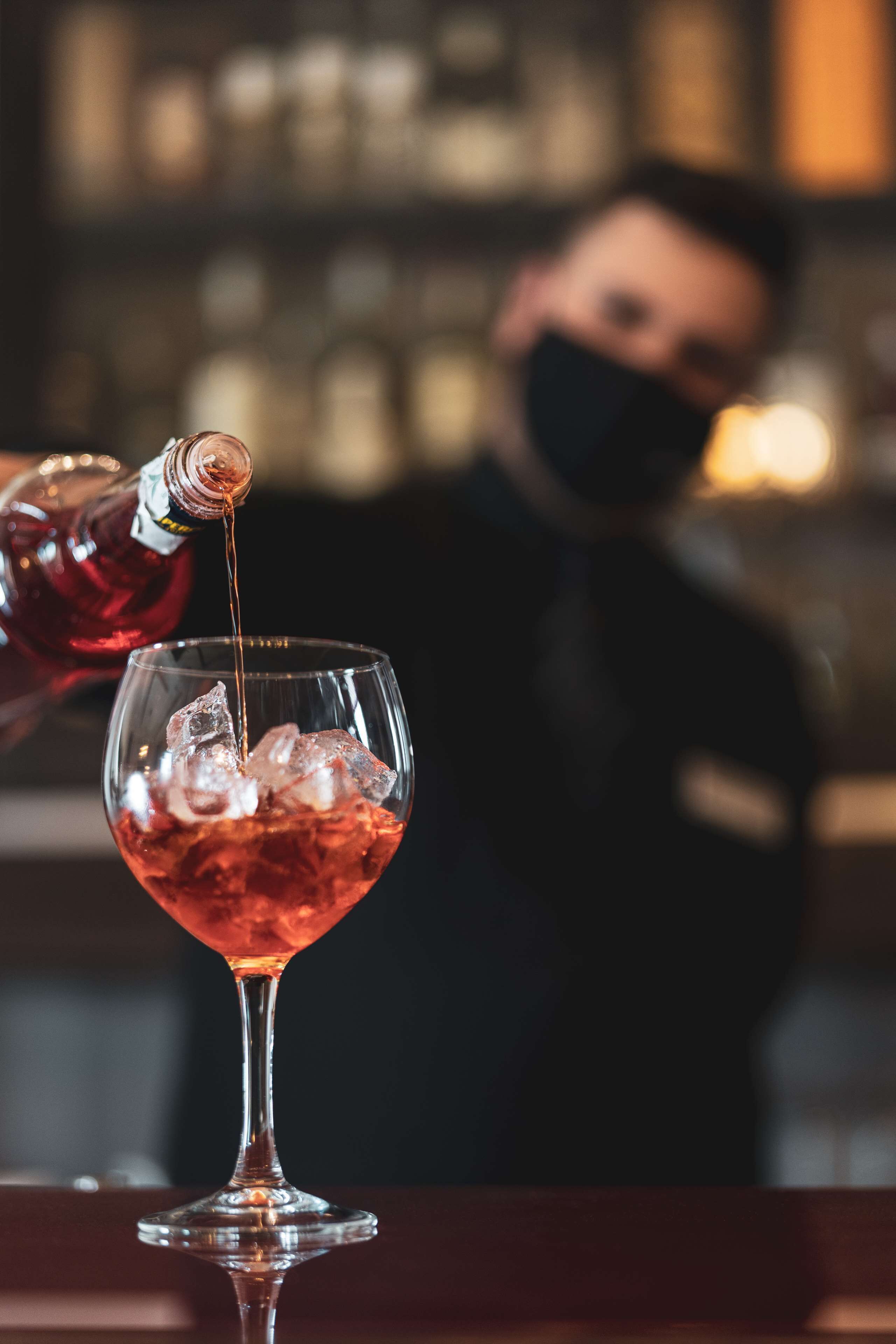 A bartender pouring a drink into a glass with ice cubes.