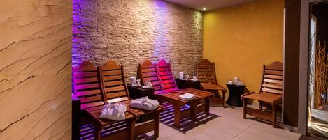A spa room with wooden massage chairs, a stone wall, and a tiled floor.