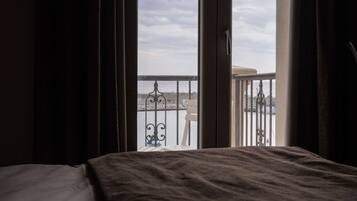 A hotel room with a bed, a balcony with a railing, and a view of the sea and a cityscape.