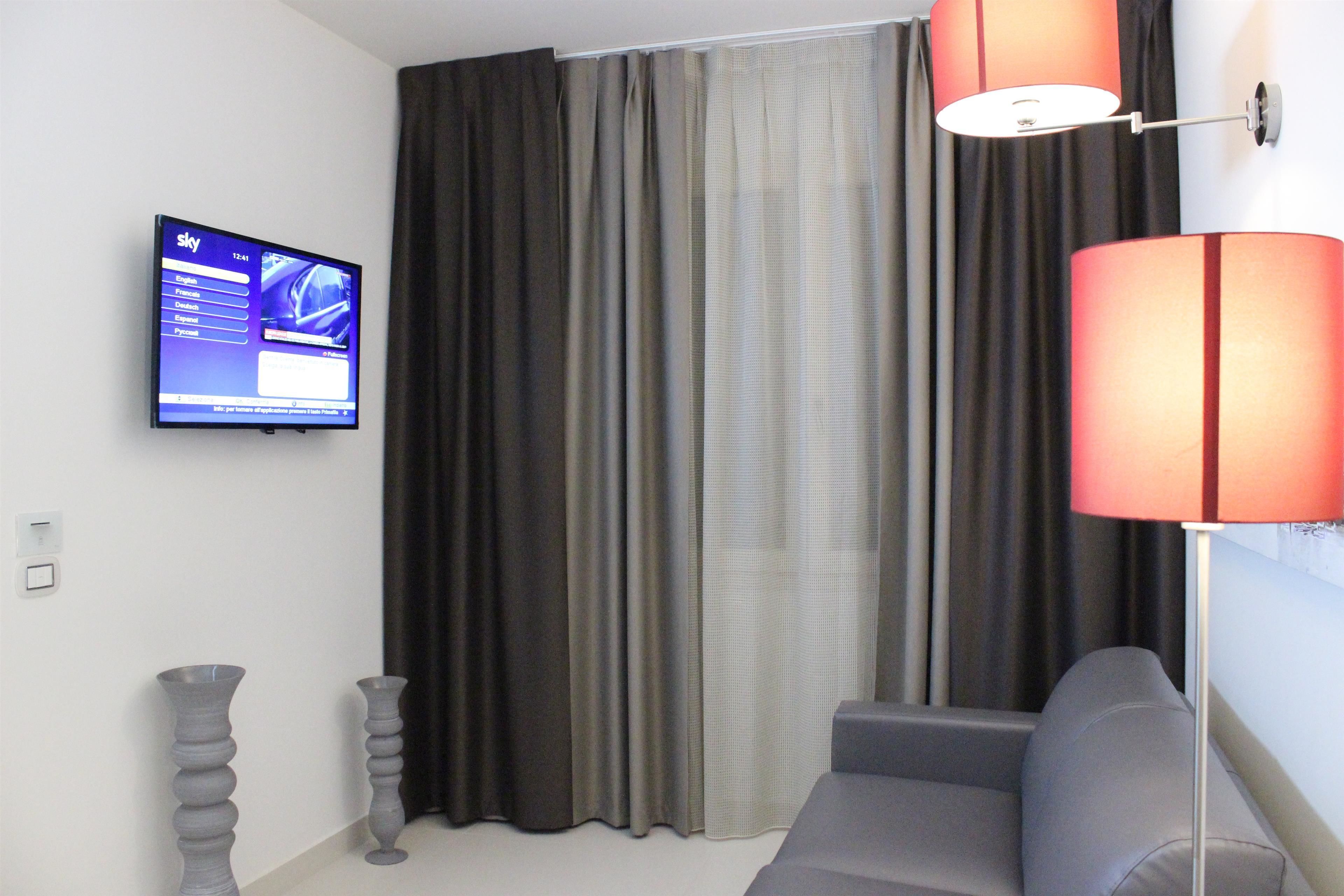 Un salón moderno con un sofá gris, un televisor de pantalla plana montado en la pared y una lámpara de pie roja.
