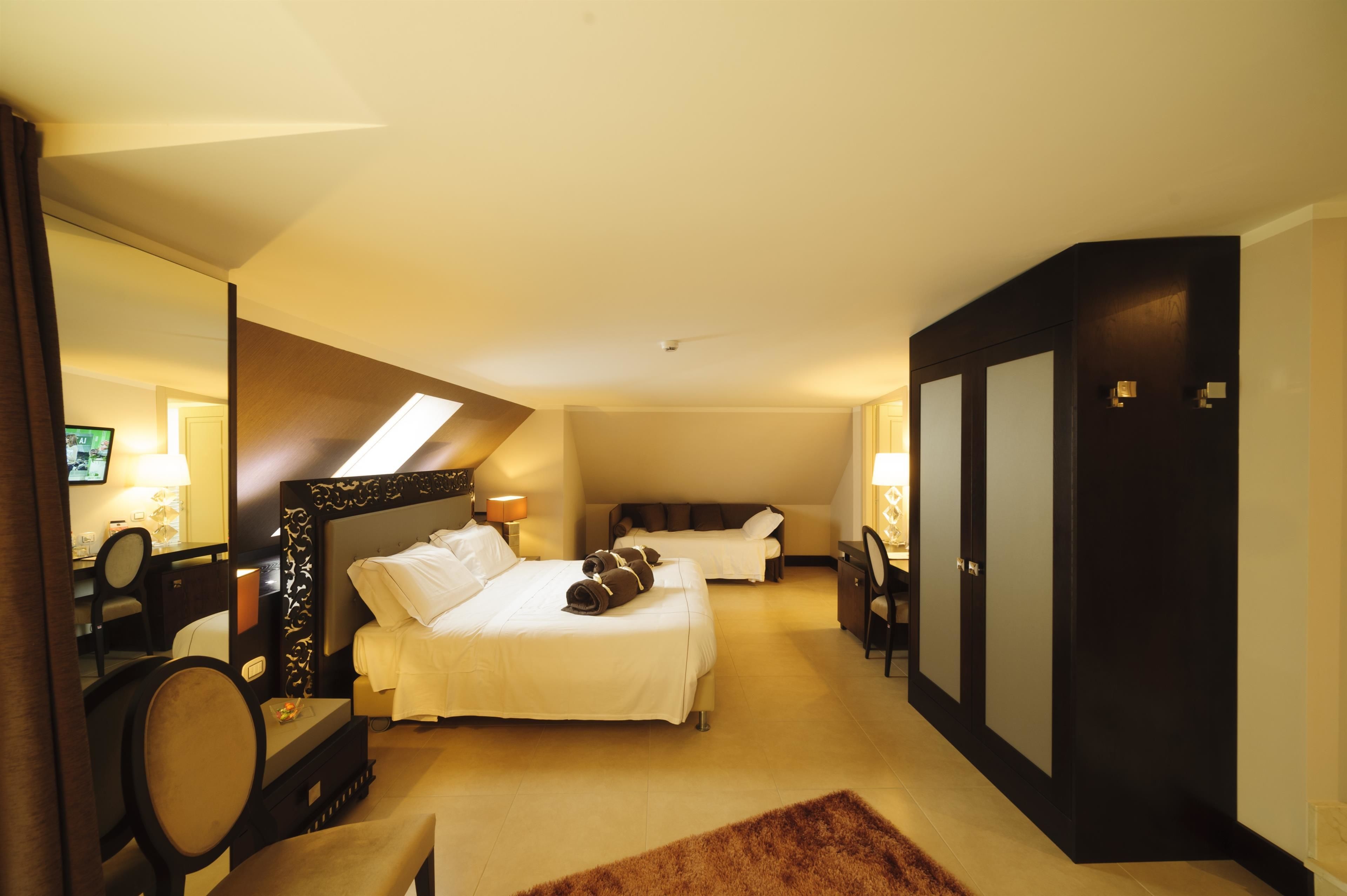 A hotel room with two beds, a desk, a chair, a wardrobe, and a mirror.