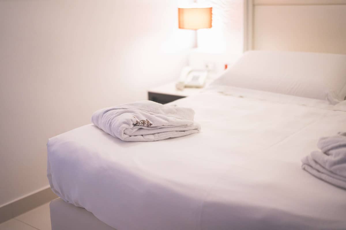 A neatly made bed with a folded towel and a bedside phone.