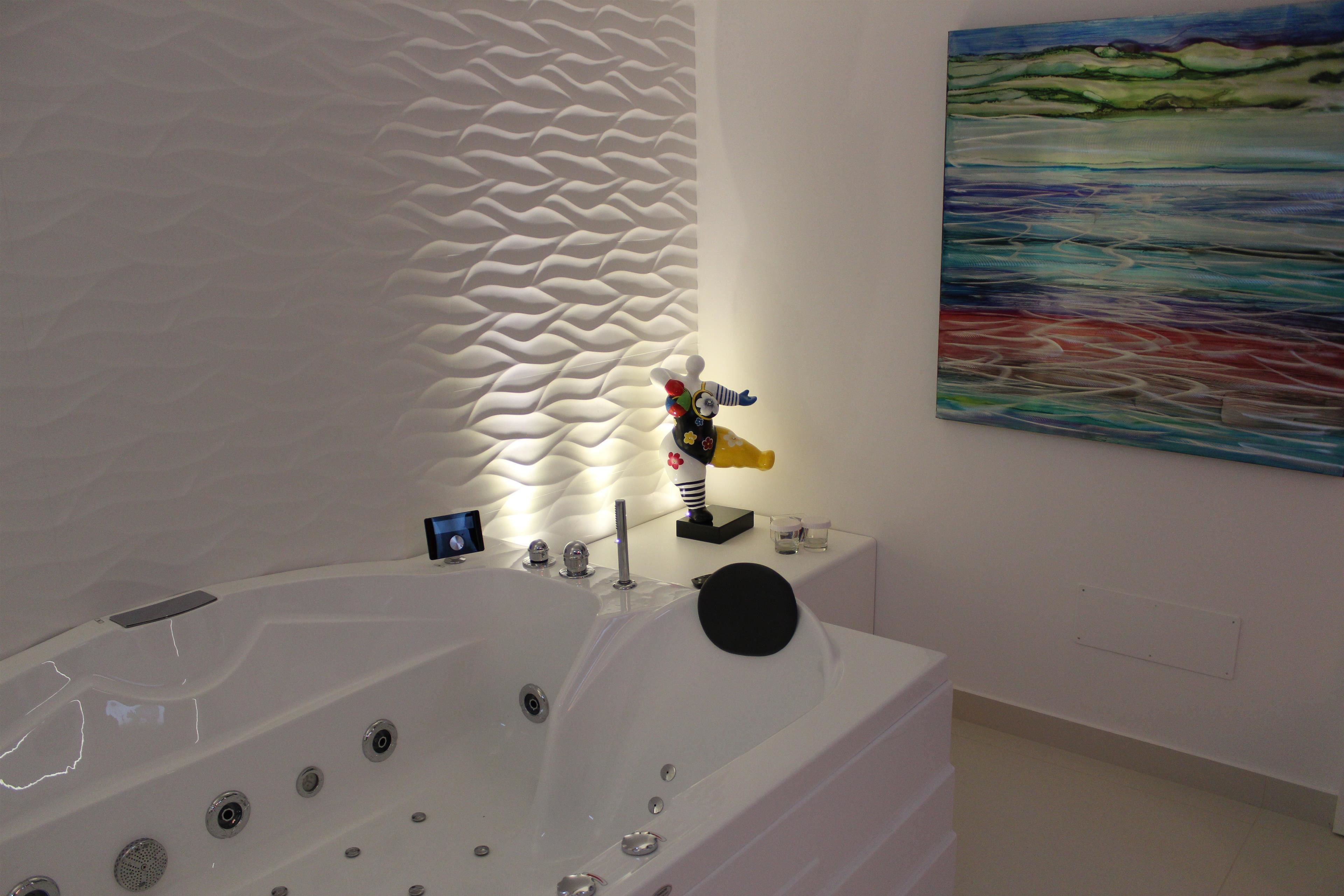 A modern bathroom with a large bathtub, a textured wall, and a painting on the wall.
