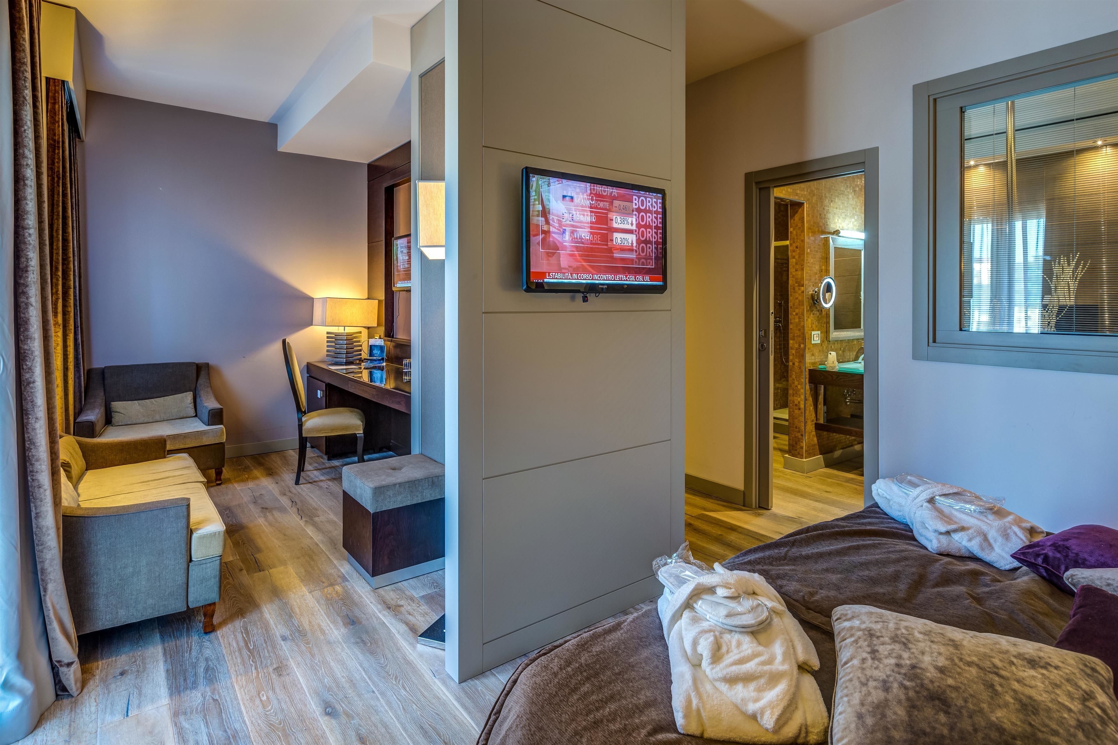 A modern hotel room with a bed, a desk, a chair, and a TV mounted on the wall.