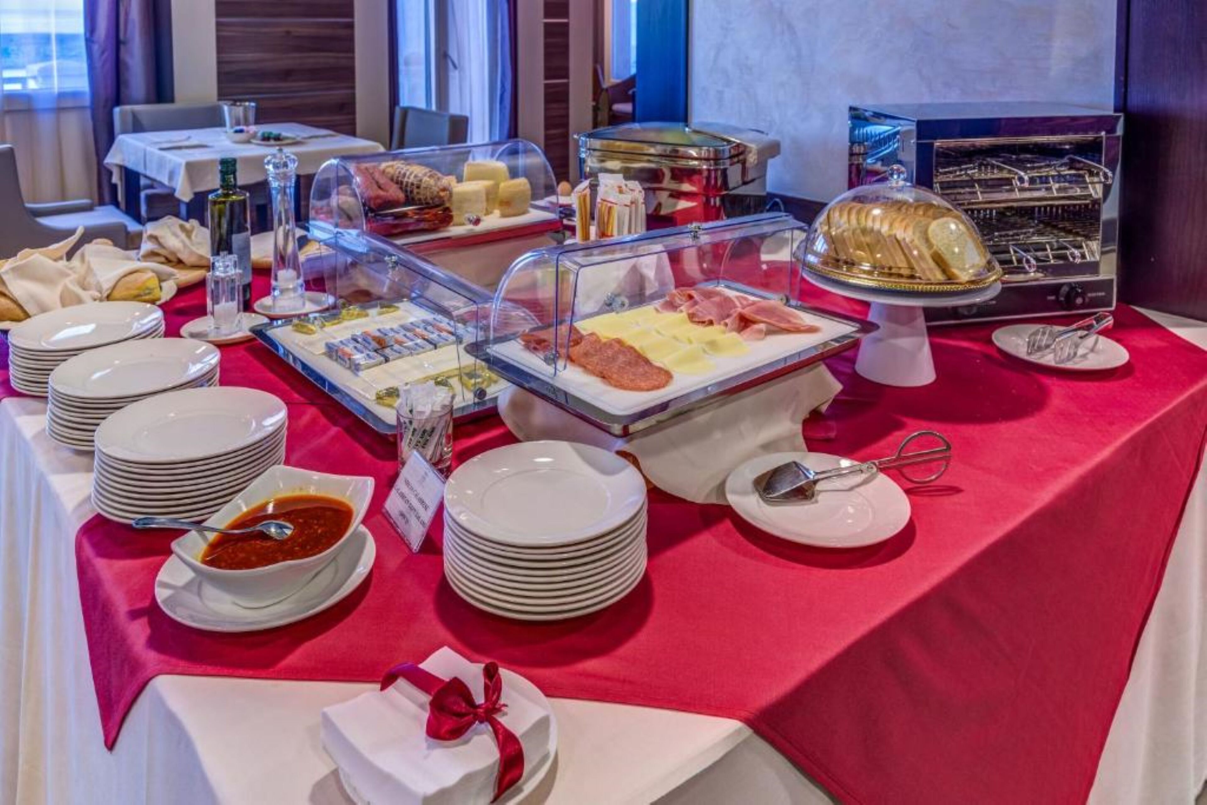 Un buffet proposant une variété de plats, notamment des viandes, des fromages et des pâtisseries, disposés sur une table recouverte d’une nappe rouge.