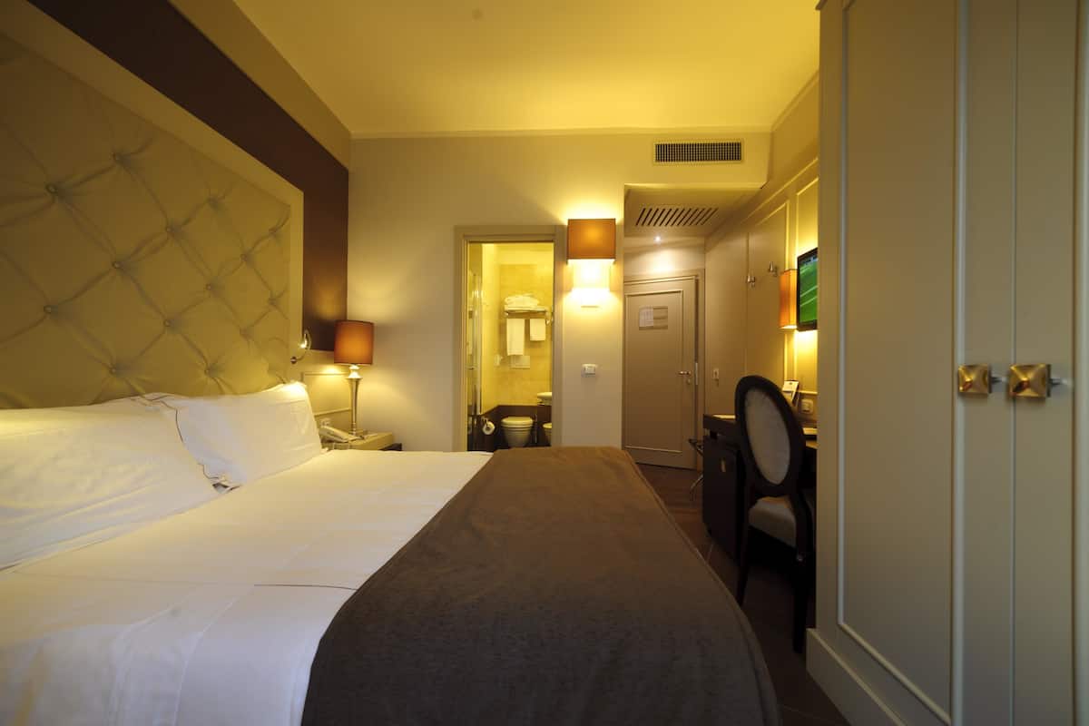 A hotel room with a large bed, a desk, and a chair. There is a bathroom visible through an open door.