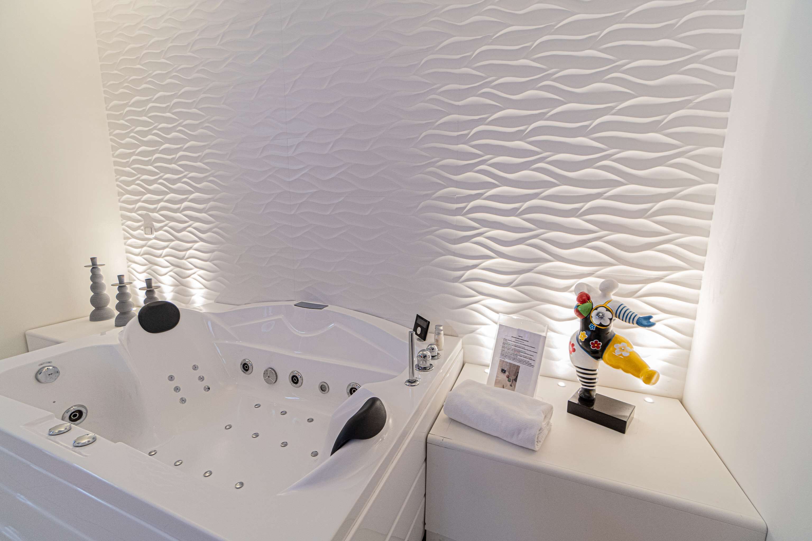 A modern bathroom with a large bathtub, a decorative wall, and a small statue on the side.