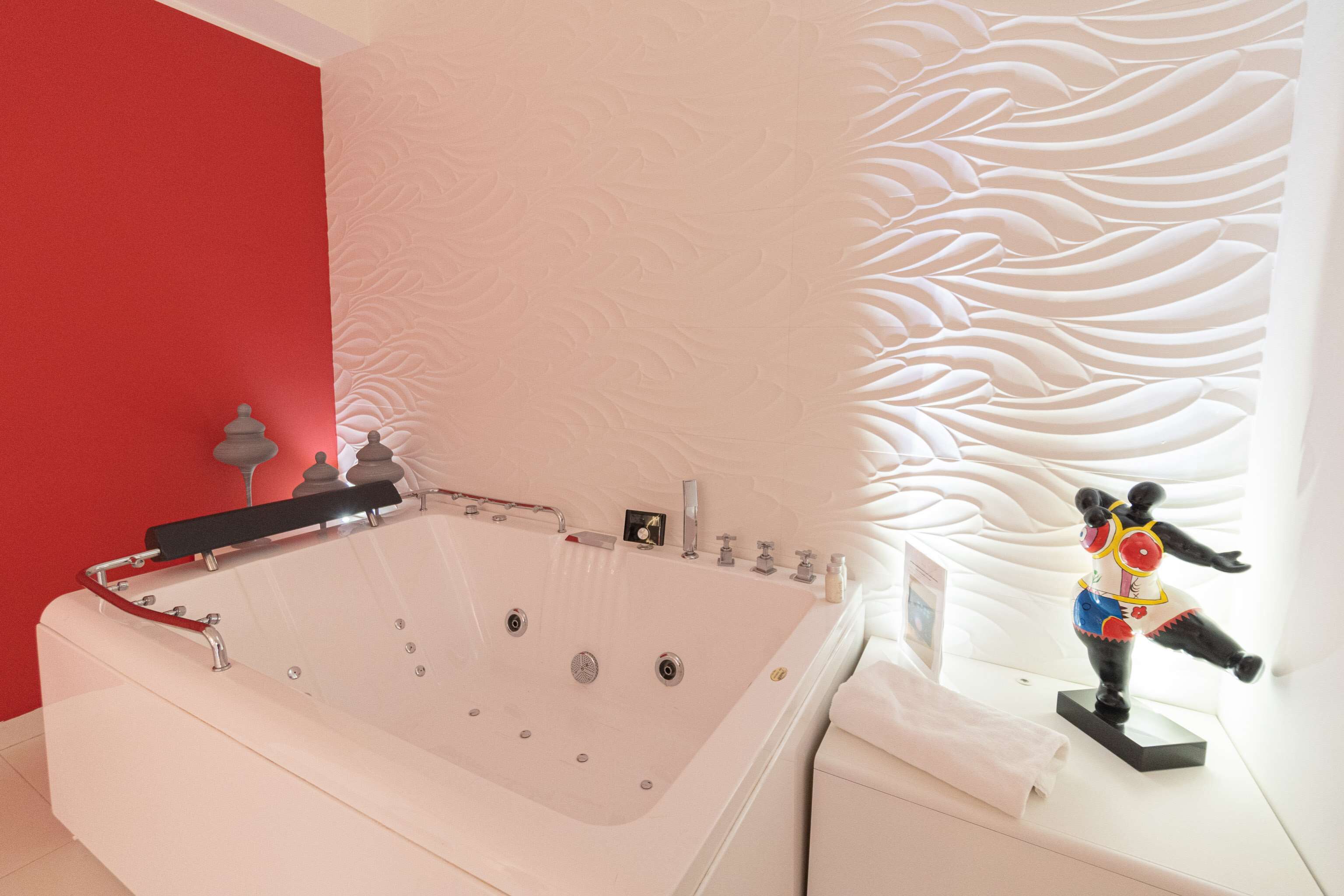 A modern bathroom with a large bathtub, a red accent wall, and a decorative wall panel.