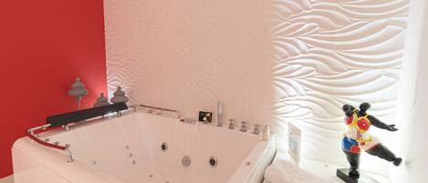 A modern bathroom with a large bathtub, a red accent wall, and a decorative wall panel.