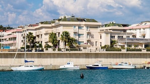 Un hotel frente al agua con varios balcones, un restaurante y un puerto deportivo con barcos.