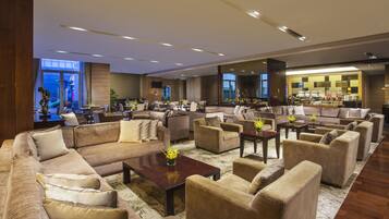 A spacious hotel lobby with multiple seating areas, a large mirror, and a view of the outdoor area.