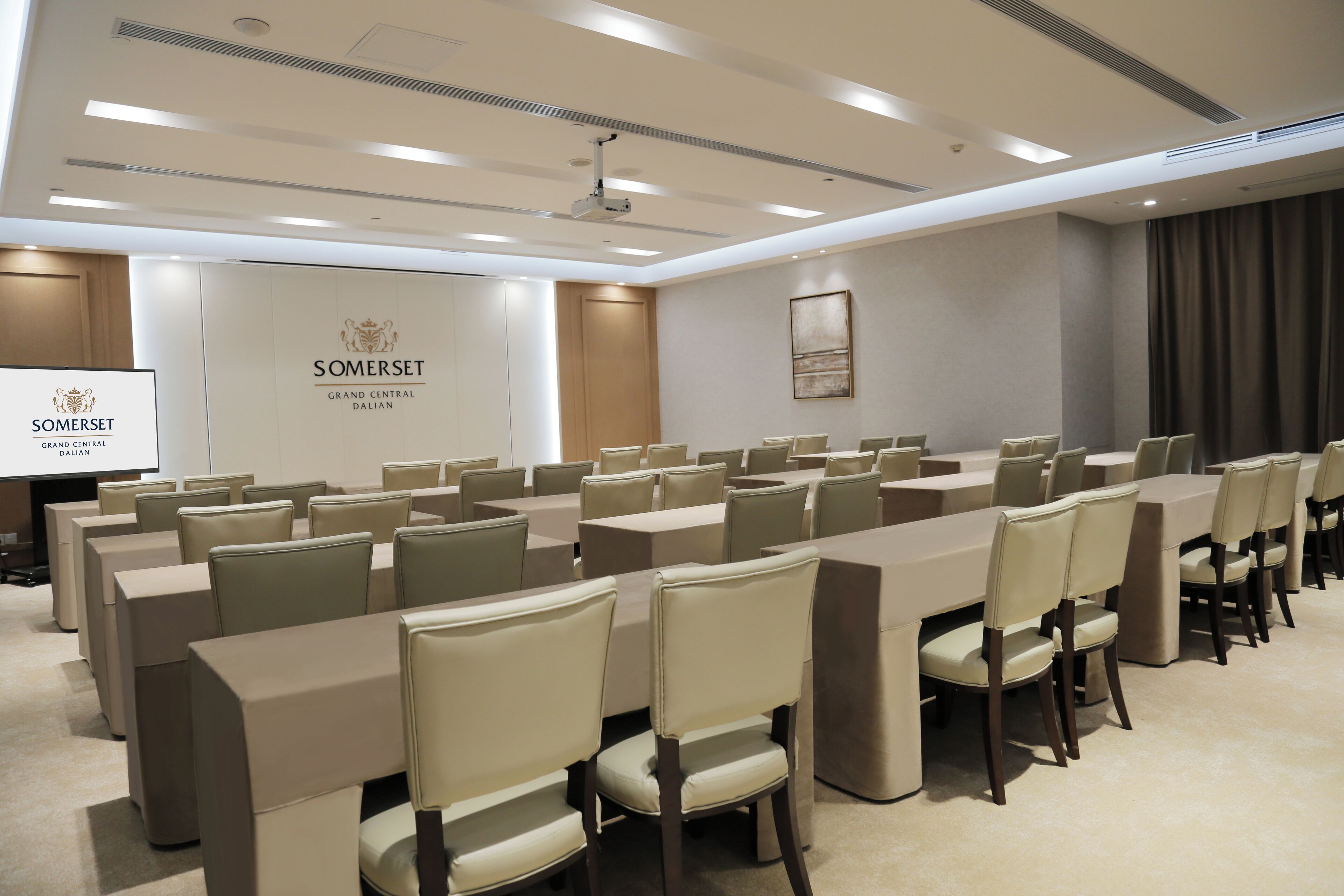 Una sala conferenze con lunghe tavolate e sedie, uno schermo per proiettore e un cartellone con su scritto "Somerset Grand Central Dalian".