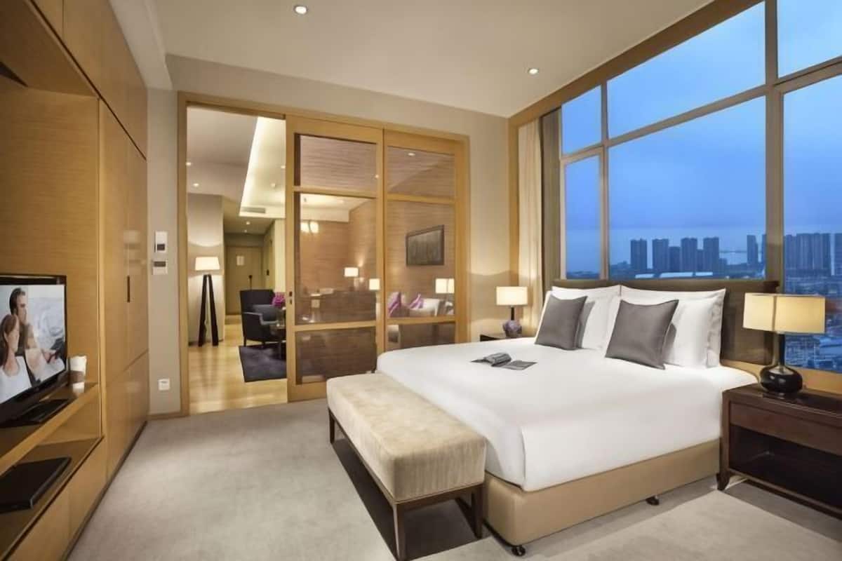 A hotel room with a large bed, a TV, a desk, and a view of the city.