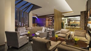 Un moderno vestíbulo de hotel con sofás, mesa de billar y vistas al horizonte de la ciudad.