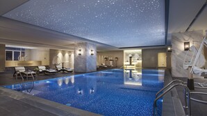 Una amplia piscina interior con techo estrellado, sillones de descanso y diseño moderno.
