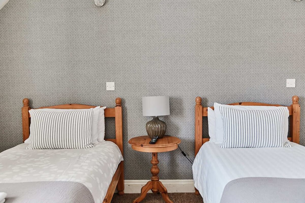Hotellihuone, jossa on kaksi sänkyä, puinen pääty, pyöreä pöytä lampun kanssa ja kuvioitu seinä.