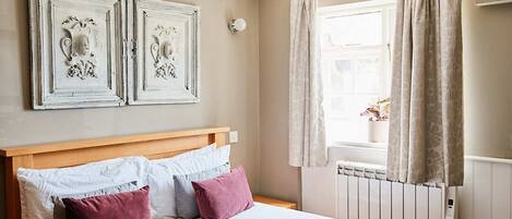 A bedroom with a wooden headboard, a bed with white and pink bedding, two wall-mounted artwork pieces, and a window with curtains.