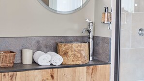 A bathroom with a round mirror, a wooden sink, a towel rack, and a bottle of shampoo. - The Bucks Head (Southampton)